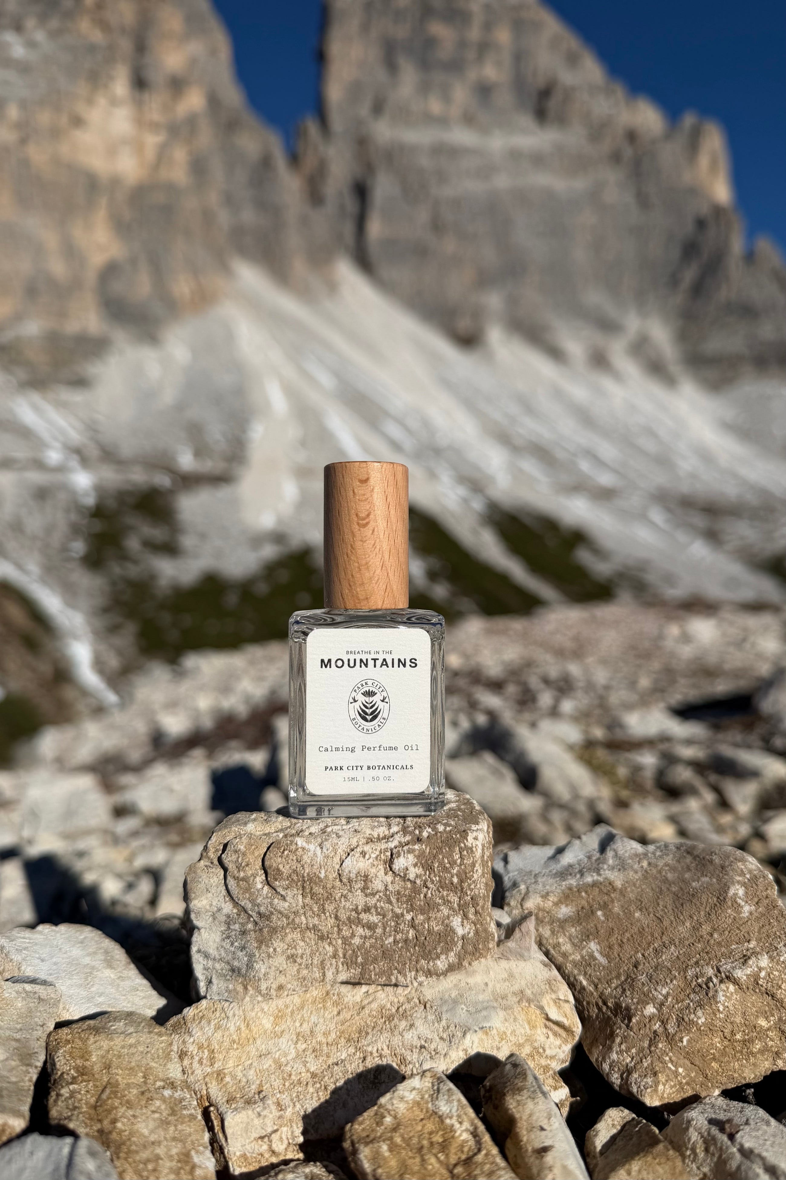 Perfume bottle with wooden cap on a rock in front of mountainous landscape