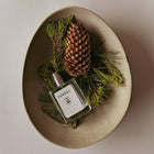 Perfume bottle labeled 'Forest' with pine cones and branches on a beige plate.